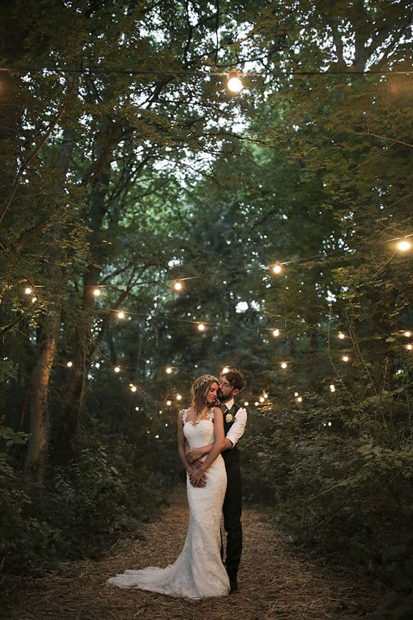 Just married couple in a wood surrounded by the fairy lights. Natural bridal beauty